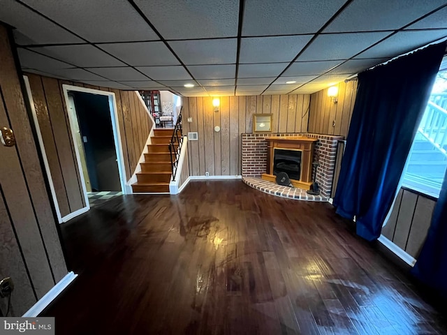 unfurnished living room with a brick fireplace, dark hardwood / wood-style floors, and a paneled ceiling