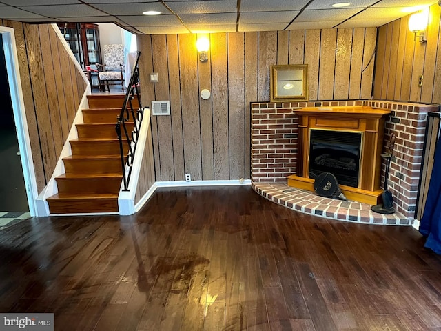 unfurnished living room with hardwood / wood-style flooring, a drop ceiling, and wood walls