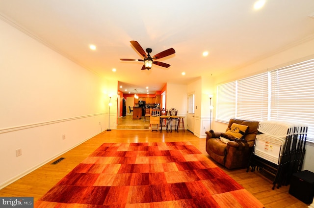 living room with ceiling fan, ornamental molding, and light hardwood / wood-style flooring