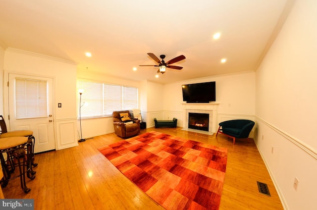 living area with crown molding, wood-type flooring, and ceiling fan