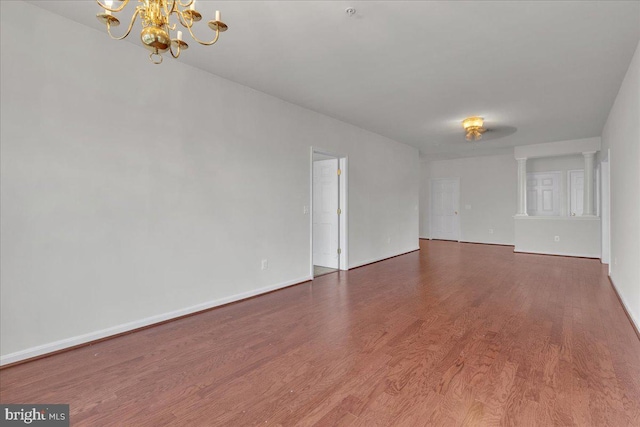 spare room with decorative columns, dark wood-type flooring, and an inviting chandelier