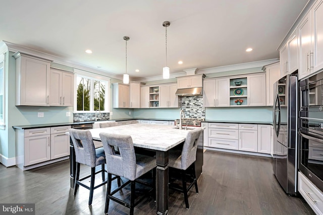 kitchen featuring black refrigerator, an island with sink, pendant lighting, wall oven, and backsplash