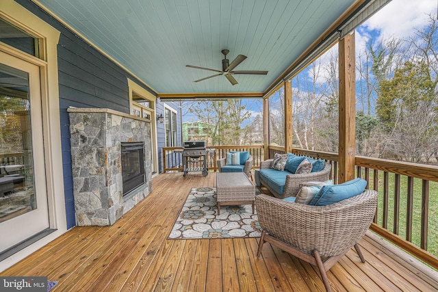 sunroom / solarium featuring wood ceiling, ceiling fan, and a stone fireplace