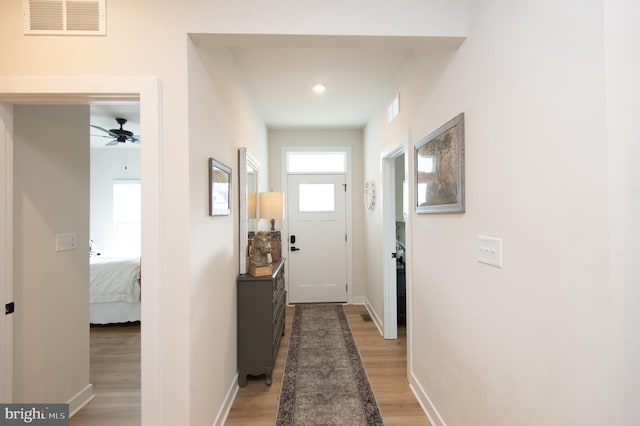 corridor with light wood finished floors, baseboards, and visible vents