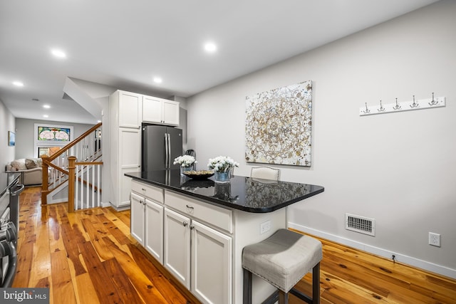 kitchen with a kitchen breakfast bar, stainless steel refrigerator, white cabinets, and light wood-type flooring