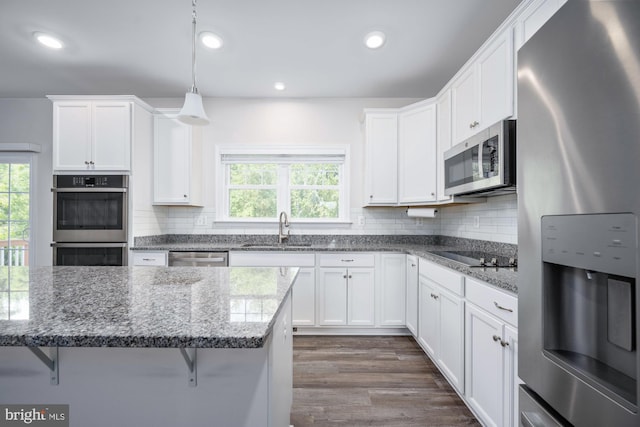 kitchen featuring pendant lighting, sink, appliances with stainless steel finishes, a kitchen breakfast bar, and white cabinets