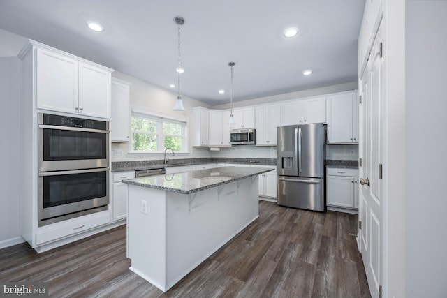 kitchen with white cabinetry, stainless steel appliances, decorative light fixtures, and a kitchen island