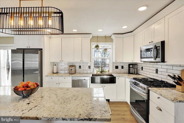 kitchen featuring sink, decorative light fixtures, white cabinets, light stone counters, and stainless steel appliances