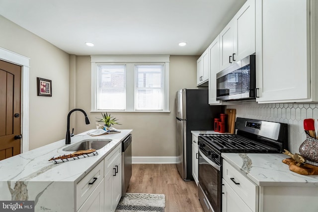 kitchen with sink, stainless steel appliances, white cabinetry, and light stone countertops