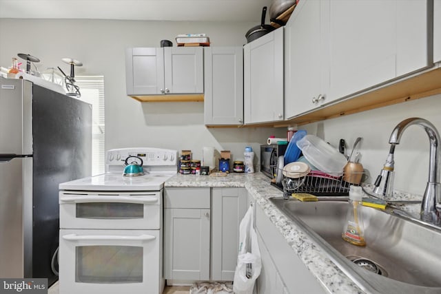 kitchen featuring range with two ovens, white cabinetry, sink, and stainless steel refrigerator