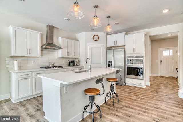 kitchen featuring wall chimney exhaust hood, sink, pendant lighting, stainless steel appliances, and white cabinets