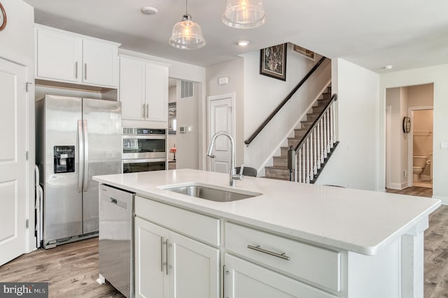 kitchen featuring pendant lighting, sink, appliances with stainless steel finishes, a kitchen island with sink, and white cabinets