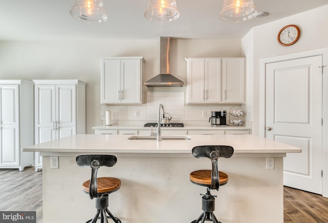 kitchen with wall chimney range hood, white cabinets, and a center island with sink