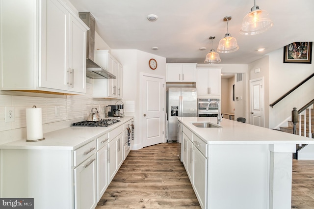 kitchen with appliances with stainless steel finishes, white cabinetry, an island with sink, sink, and hanging light fixtures