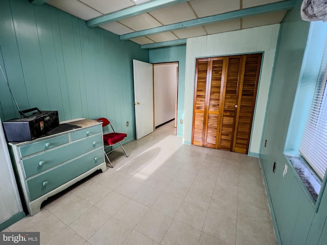 bedroom featuring beamed ceiling, a closet, and wood walls