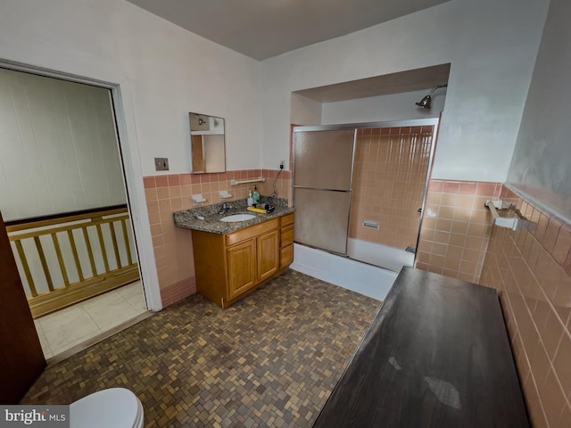 full bathroom with tile patterned floors, toilet, bath / shower combo with glass door, tile walls, and vanity