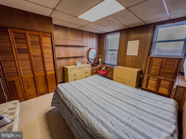 bedroom featuring a paneled ceiling, tile patterned floors, a closet, and wood walls