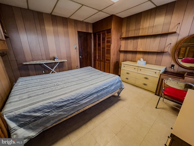 bedroom with wooden walls, a closet, and a drop ceiling