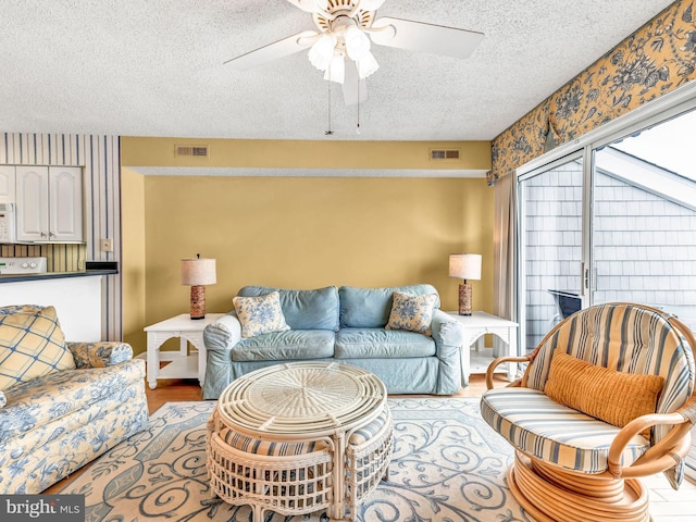 living room featuring ceiling fan, light wood-type flooring, and a textured ceiling