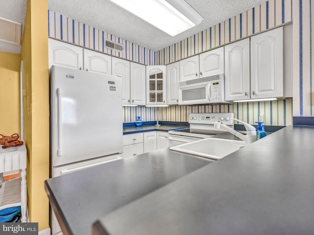 kitchen with white cabinetry, a textured ceiling, white appliances, and kitchen peninsula