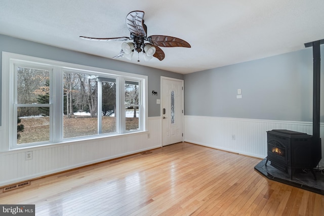 unfurnished living room with a wood stove, ceiling fan, and light hardwood / wood-style flooring