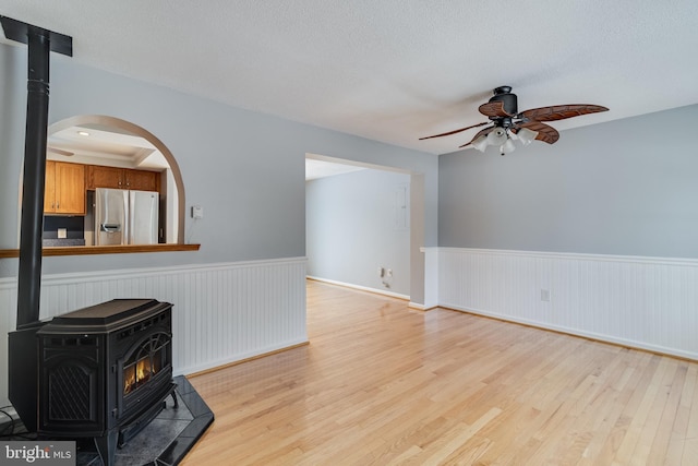 unfurnished living room with ceiling fan, light hardwood / wood-style flooring, a textured ceiling, and a wood stove