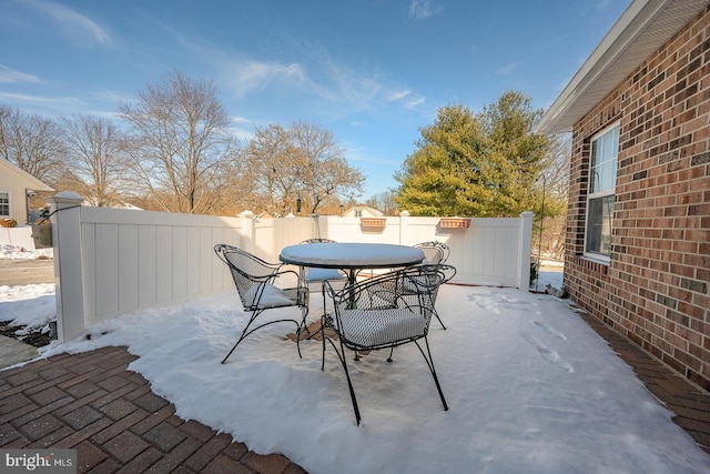 snow covered patio with outdoor dining area and a fenced backyard