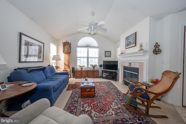 carpeted living room with ceiling fan, a tile fireplace, and vaulted ceiling