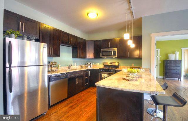 kitchen featuring a breakfast bar area, appliances with stainless steel finishes, dark hardwood / wood-style flooring, kitchen peninsula, and pendant lighting