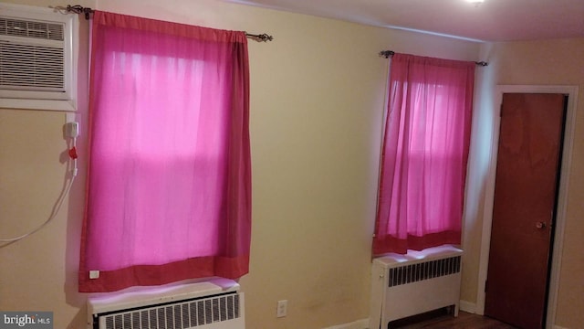 interior space with radiator heating unit, multiple windows, and a wall unit AC