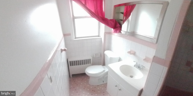 bathroom with radiator heating unit, a healthy amount of sunlight, toilet, and tile walls