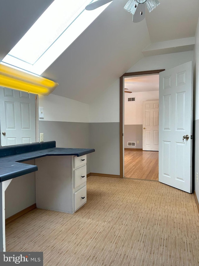 kitchen with white cabinetry, ceiling fan, light hardwood / wood-style floors, and vaulted ceiling with skylight