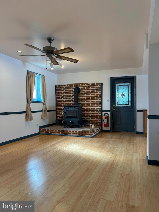 unfurnished living room with ceiling fan, a wood stove, and light wood-type flooring