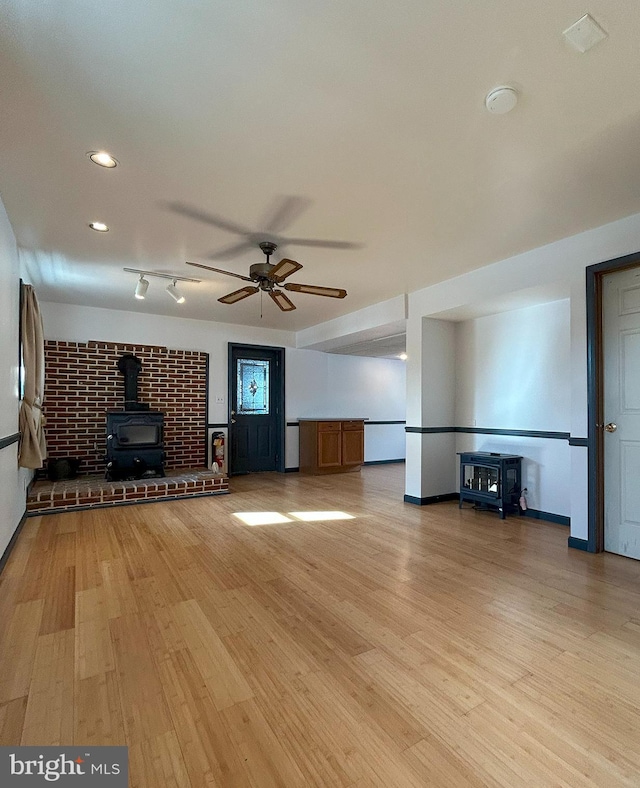 unfurnished living room with ceiling fan, a wood stove, and light wood-type flooring