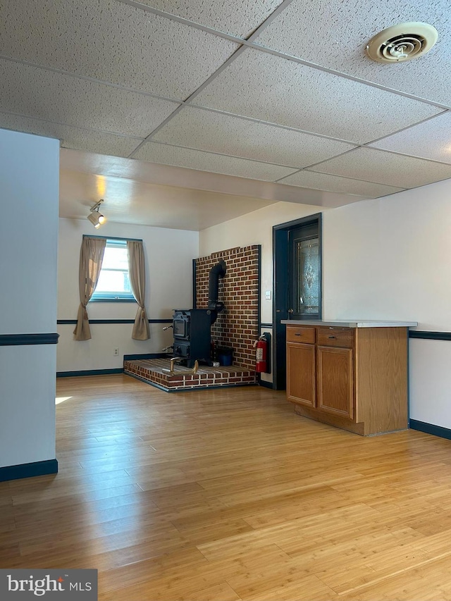 interior space featuring a paneled ceiling, a wood stove, and light wood-type flooring