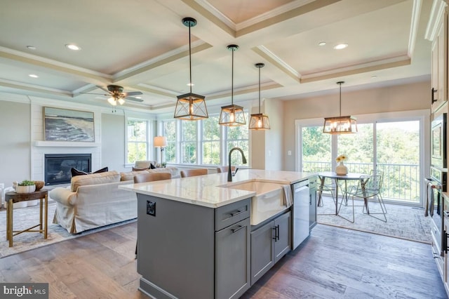 kitchen featuring sink, light stone counters, hanging light fixtures, gray cabinets, and a kitchen island with sink