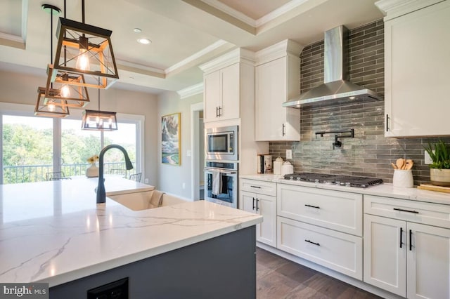 kitchen with wall chimney exhaust hood, white cabinetry, stainless steel appliances, and hanging light fixtures