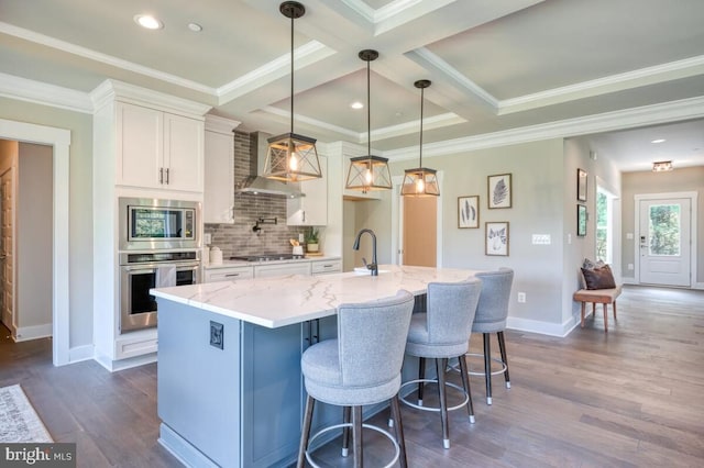 kitchen with appliances with stainless steel finishes, pendant lighting, white cabinetry, a large island, and wall chimney range hood