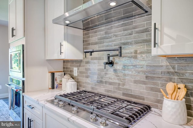 kitchen featuring white cabinetry, appliances with stainless steel finishes, wall chimney range hood, and backsplash