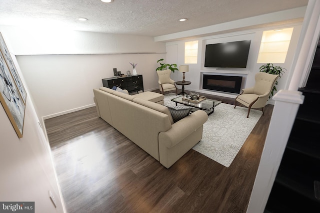 living room with dark wood-type flooring, baseboards, recessed lighting, a glass covered fireplace, and a textured ceiling