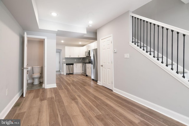 interior space featuring white cabinets, stainless steel appliances, light hardwood / wood-style floors, and backsplash