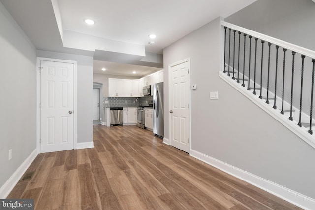 interior space featuring white cabinets, stainless steel appliances, light hardwood / wood-style floors, and tasteful backsplash