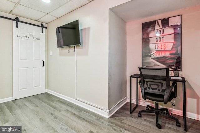 home office with a barn door, a paneled ceiling, and wood-type flooring