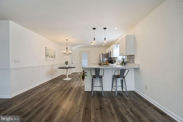 kitchen with white cabinetry, decorative light fixtures, a kitchen breakfast bar, kitchen peninsula, and stainless steel appliances