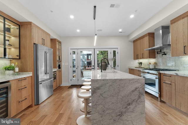 kitchen featuring premium appliances, wine cooler, a spacious island, wall chimney exhaust hood, and decorative backsplash