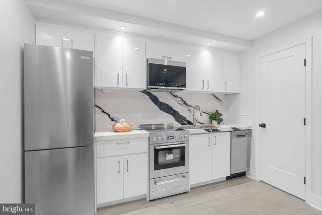 kitchen with appliances with stainless steel finishes, decorative backsplash, white cabinets, light wood-type flooring, and sink