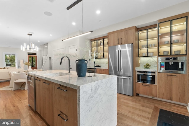 kitchen with appliances with stainless steel finishes, an island with sink, light hardwood / wood-style floors, sink, and hanging light fixtures