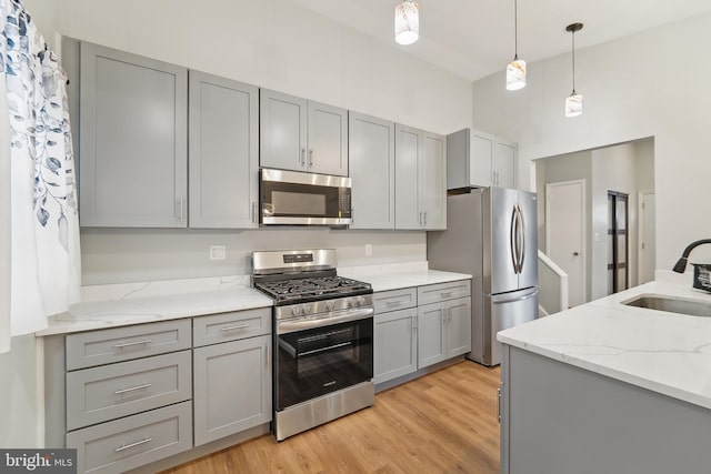 kitchen featuring appliances with stainless steel finishes, sink, hanging light fixtures, light stone counters, and gray cabinetry