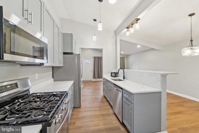 kitchen with hanging light fixtures, appliances with stainless steel finishes, sink, light wood-type flooring, and light stone counters