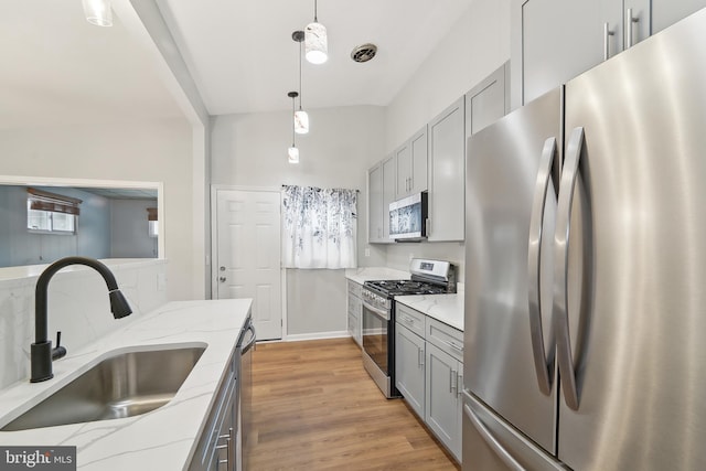 kitchen with light stone countertops, appliances with stainless steel finishes, sink, hanging light fixtures, and gray cabinetry